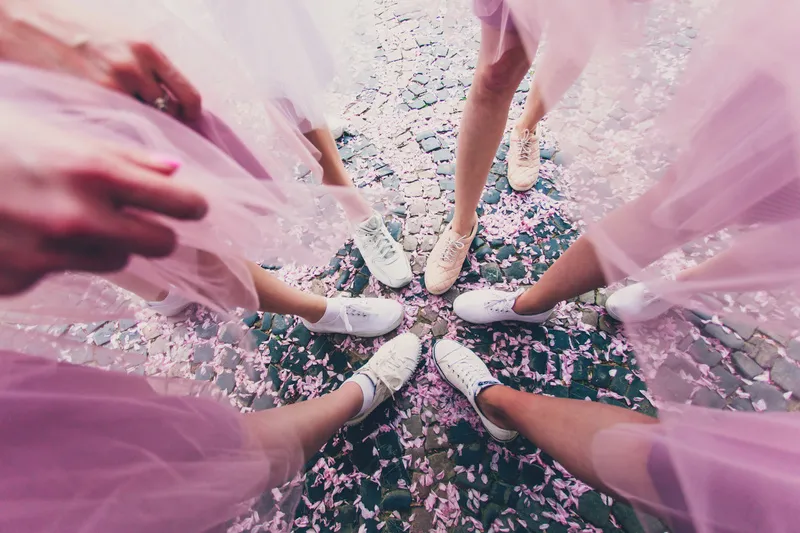 noiva e madrinhas posam com os pés ao centro enquanto usam tênis branco e saia de tule rosa combinando