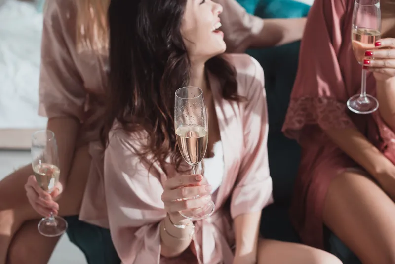 Noiva e amigas em robes rosas combinando sorriem enquanto bebem champagne
